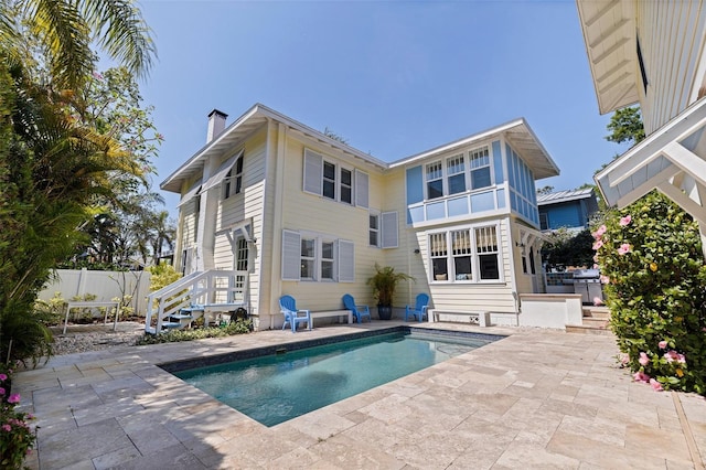 rear view of property with fence, a chimney, a patio area, and a fenced in pool