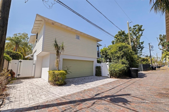 view of home's exterior with driveway, fence, a gate, an attached garage, and stucco siding