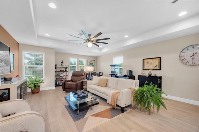living room with a wealth of natural light, a raised ceiling, a ceiling fan, and light wood finished floors