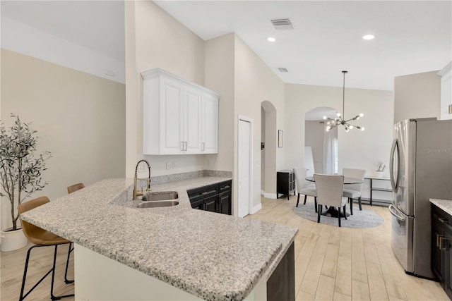 kitchen with an inviting chandelier, a sink, light wood-type flooring, arched walkways, and freestanding refrigerator
