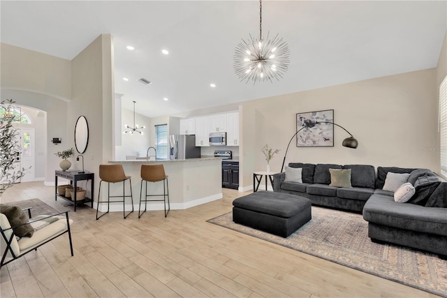 living area featuring visible vents, a chandelier, light wood-style floors, arched walkways, and high vaulted ceiling