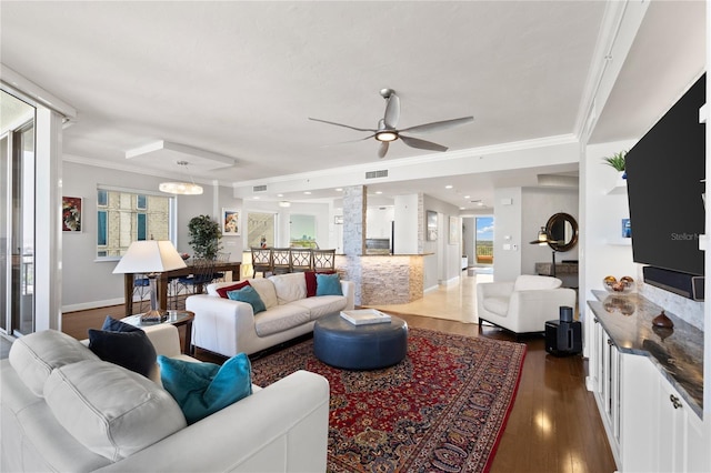 living area with crown molding, visible vents, baseboards, dark wood-style flooring, and a ceiling fan