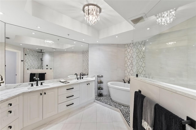 bathroom featuring double vanity, tile walls, a freestanding tub, a sink, and a raised ceiling