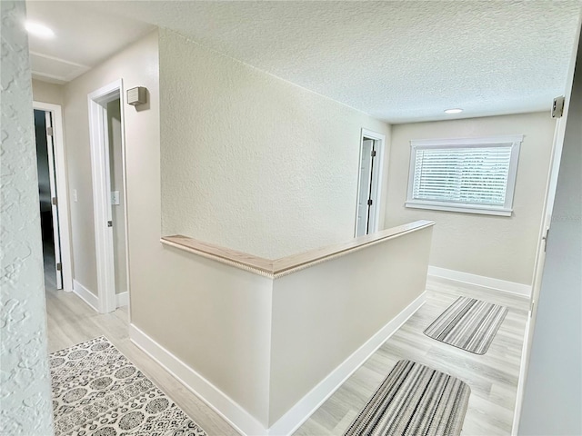 592 Ken Hubbard Rd, Terra Ceia, FL 34250 - hallway featuring light wood-style flooring, a textured wall, a textured ceiling, baseboards, and an upstairs landing