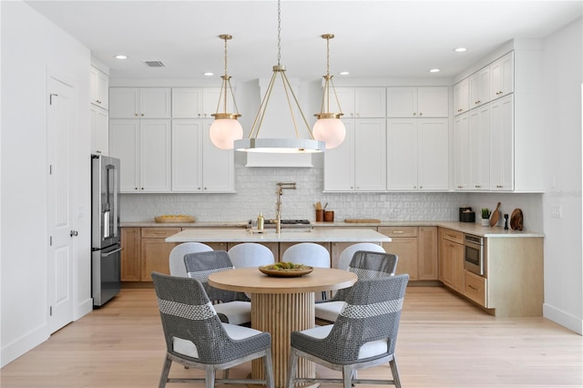 kitchen with light wood-style flooring, stainless steel appliances, light countertops, premium range hood, and a kitchen island with sink