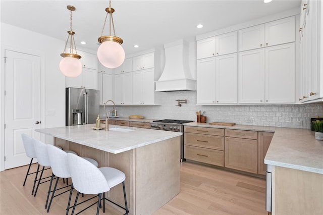 kitchen with light wood finished floors, a sink, custom range hood, high end appliances, and backsplash