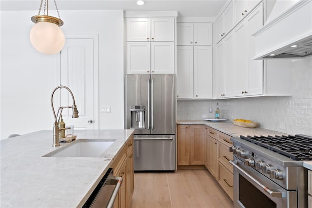 kitchen with light stone countertops, high end appliances, light wood-style flooring, a sink, and premium range hood
