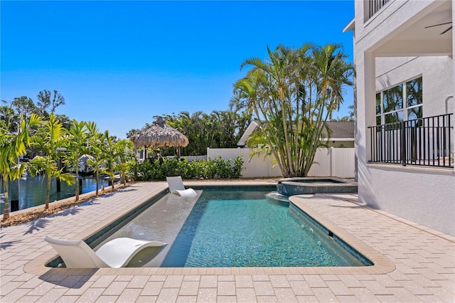 view of pool with a patio, a water view, ceiling fan, a fenced backyard, and a pool with connected hot tub