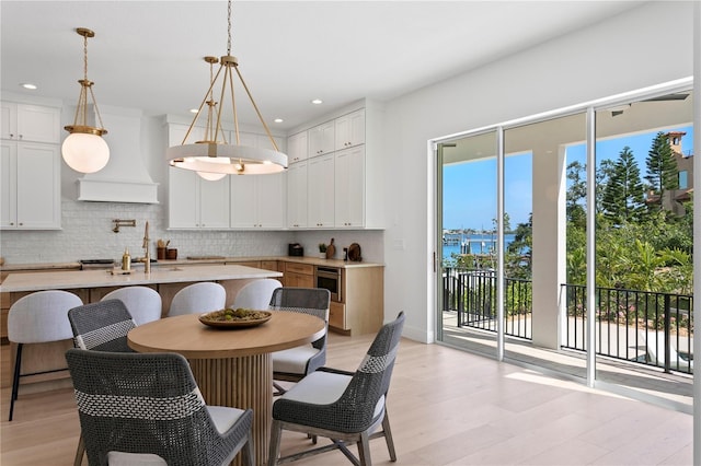 kitchen featuring light countertops, light wood-type flooring, custom exhaust hood, an island with sink, and backsplash