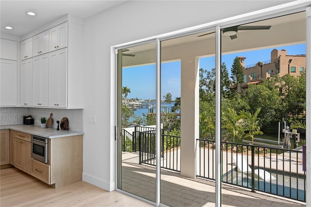 doorway with light wood-style floors, ceiling fan, a water view, baseboards, and recessed lighting