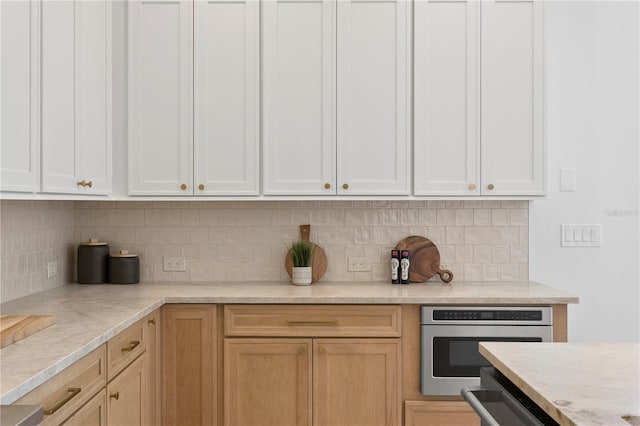 kitchen with white cabinetry, light stone countertops, oven, and decorative backsplash