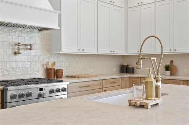 kitchen featuring stainless steel range with gas cooktop, custom exhaust hood, decorative backsplash, and white cabinets