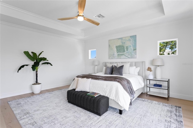 bedroom with wood finished floors, visible vents, crown molding, and a tray ceiling