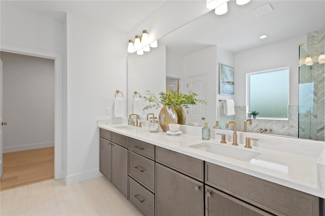 bathroom with double vanity, baseboards, a shower, and a sink