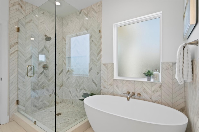 full bathroom featuring a healthy amount of sunlight, a stall shower, tile walls, a freestanding tub, and wainscoting