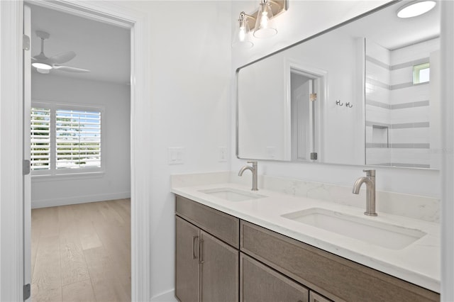 full bath with double vanity, a sink, a ceiling fan, and wood finished floors