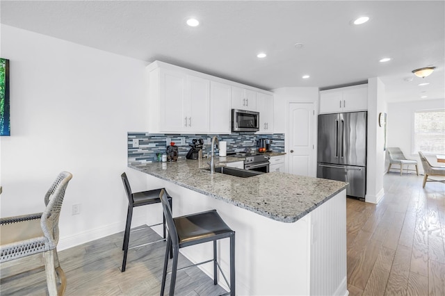 100 Windrush Blvd Unit 1, Indian Rocks Beach, FL 33785 - kitchen featuring appliances with stainless steel finishes, light stone counters, a peninsula, a sink, and backsplash