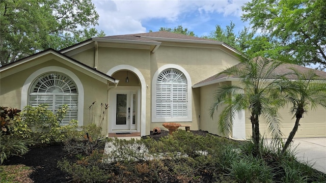 property entrance with a shingled roof, an attached garage, driveway, and stucco siding