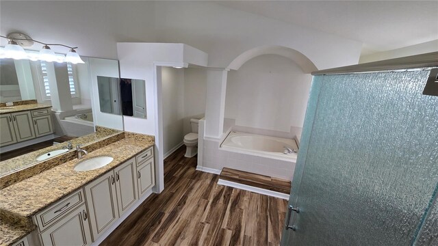full bath with a sink, toilet, two vanities, wood finished floors, and a garden tub
