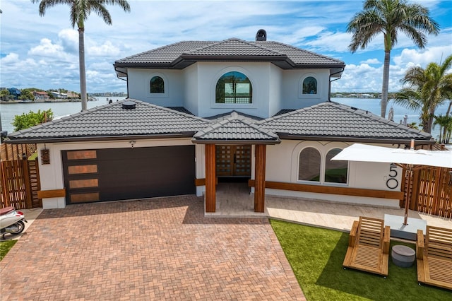 mediterranean / spanish-style home with a tile roof, an attached garage, decorative driveway, stucco siding, and french doors