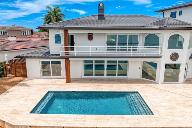 back of house featuring a chimney, stucco siding, a tiled roof, a patio area, and a balcony