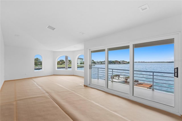 unfurnished room featuring vaulted ceiling, light colored carpet, visible vents, and a water view