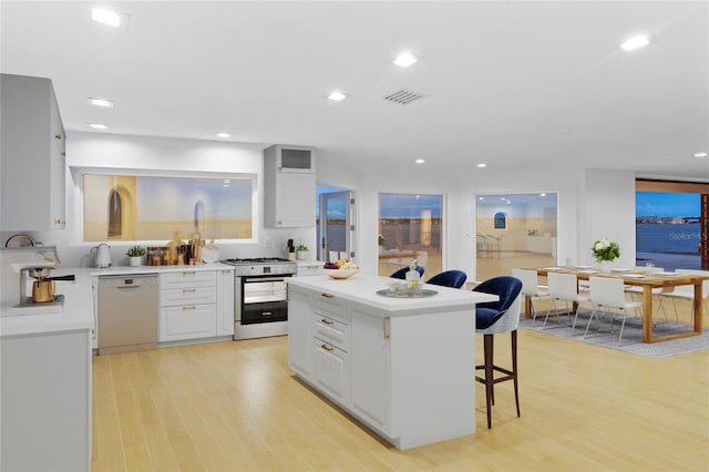 kitchen featuring a breakfast bar area, light wood-style floors, dishwasher, visible vents, and stainless steel range with gas cooktop
