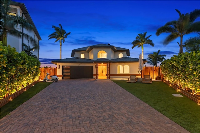 view of front of property featuring fence, a tiled roof, decorative driveway, an attached garage, and stucco siding