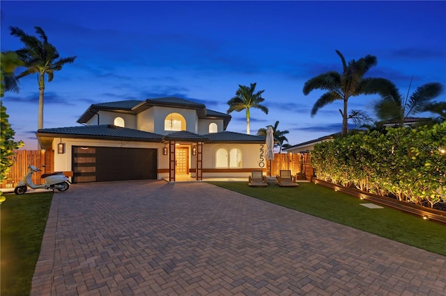 view of front of home with stucco siding, decorative driveway, a tiled roof, an attached garage, and fence