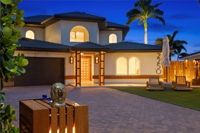 mediterranean / spanish-style home featuring stucco siding, a tiled roof, fence, decorative driveway, and a garage