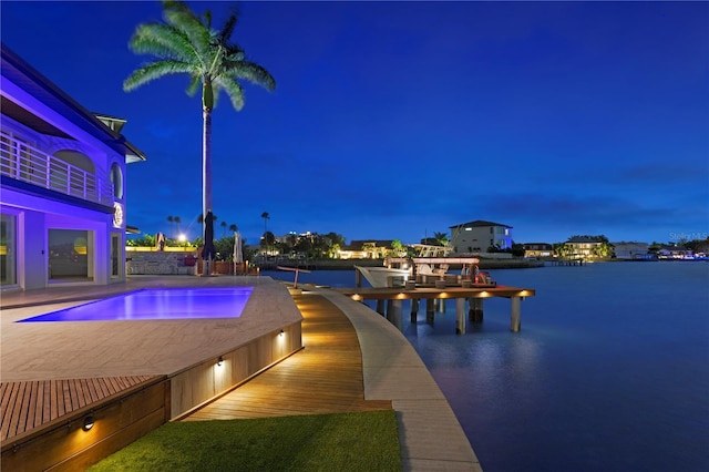 pool at night featuring a water view, a dock, and an in ground hot tub