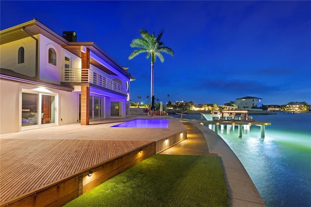 pool at night featuring a water view, an infinity pool, and a patio area