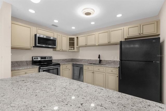 kitchen featuring glass insert cabinets, cream cabinets, black appliances, a sink, and visible vents