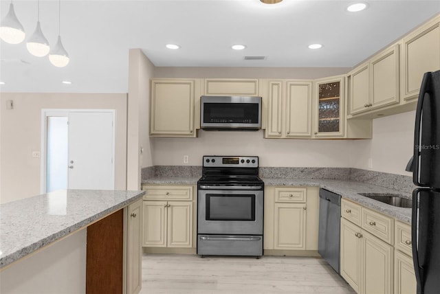 kitchen with stainless steel appliances, glass insert cabinets, light wood-type flooring, cream cabinets, and light stone counters