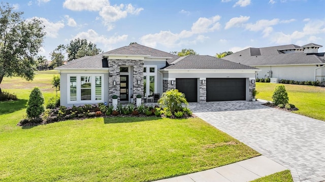 prairie-style home with a front yard, a garage, a shingled roof, decorative driveway, and stone siding