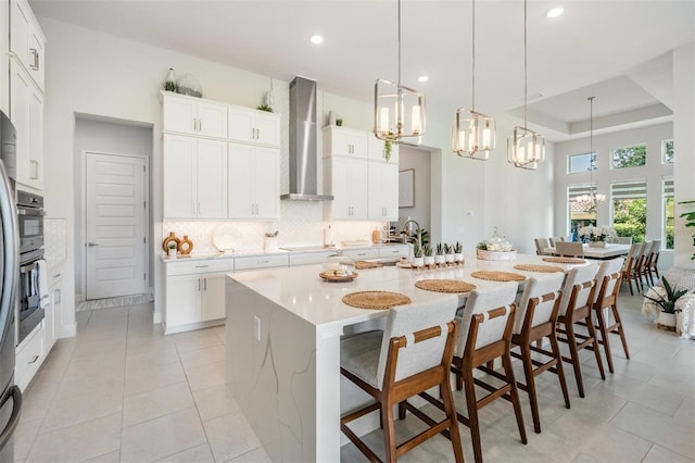 kitchen with tasteful backsplash, a notable chandelier, wall chimney exhaust hood, and a kitchen breakfast bar