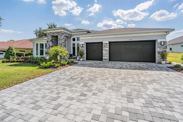prairie-style house with stone siding, decorative driveway, a front yard, stucco siding, and a garage