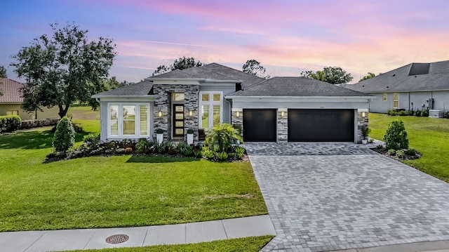 view of front facade featuring decorative driveway, a front lawn, stone siding, and an attached garage