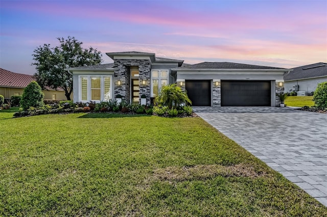 prairie-style house with decorative driveway, a lawn, stone siding, and an attached garage