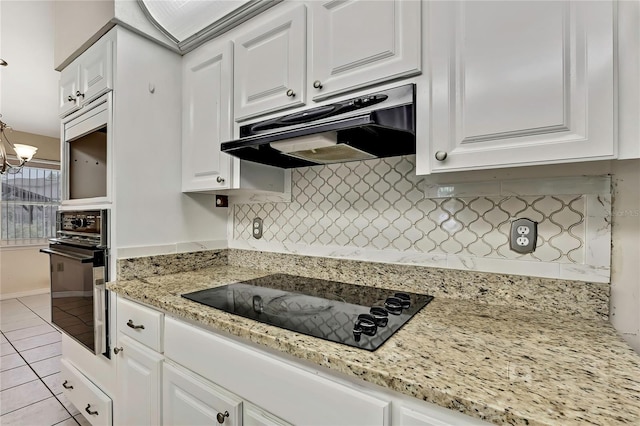 kitchen featuring under cabinet range hood, light tile patterned flooring, black appliances, backsplash, and white cabinetry