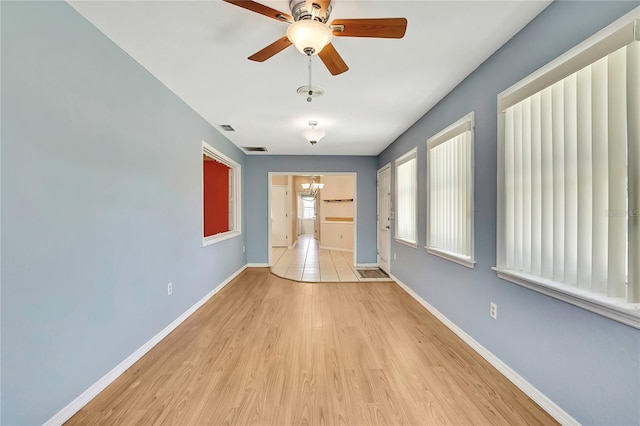interior space with baseboards, light wood-type flooring, visible vents, and ceiling fan with notable chandelier