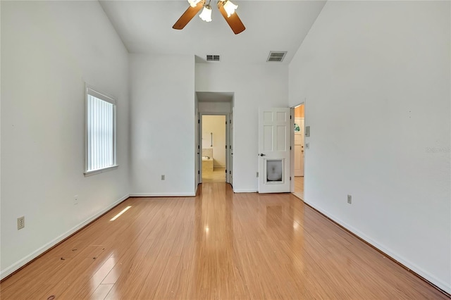 unfurnished bedroom featuring visible vents, baseboards, light wood finished floors, and a high ceiling