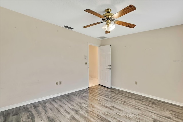 spare room with a ceiling fan, visible vents, wood finished floors, and baseboards