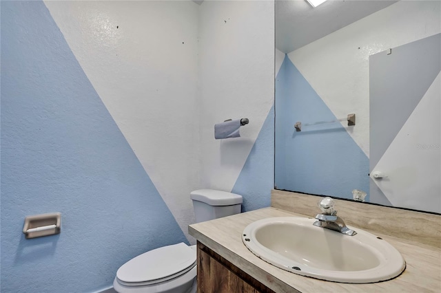 bathroom with toilet, a textured wall, and vanity