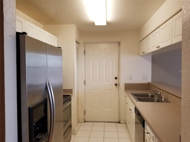 kitchen featuring light tile patterned floors, appliances with stainless steel finishes, white cabinets, a sink, and a textured ceiling
