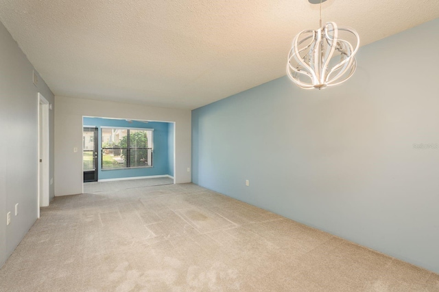 spare room with a textured ceiling, a notable chandelier, and light colored carpet