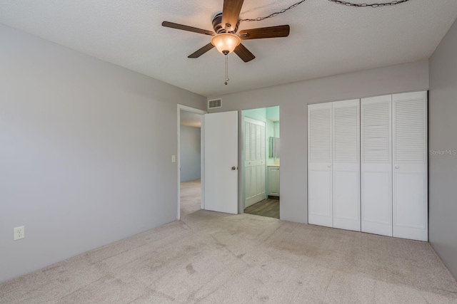 unfurnished bedroom featuring a closet, carpet, ensuite bathroom, visible vents, and a ceiling fan