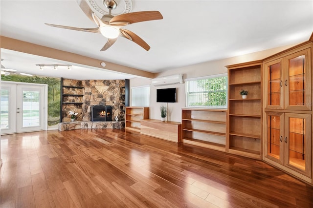 unfurnished living room featuring a fireplace, a wall mounted air conditioner, french doors, a ceiling fan, and wood finished floors