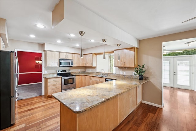 kitchen with light brown cabinetry, a sink, light wood finished floors, a peninsula, and stainless steel appliances