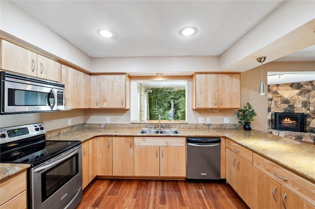 kitchen featuring light brown cabinetry, dark wood-style flooring, appliances with stainless steel finishes, a sink, and a stone fireplace